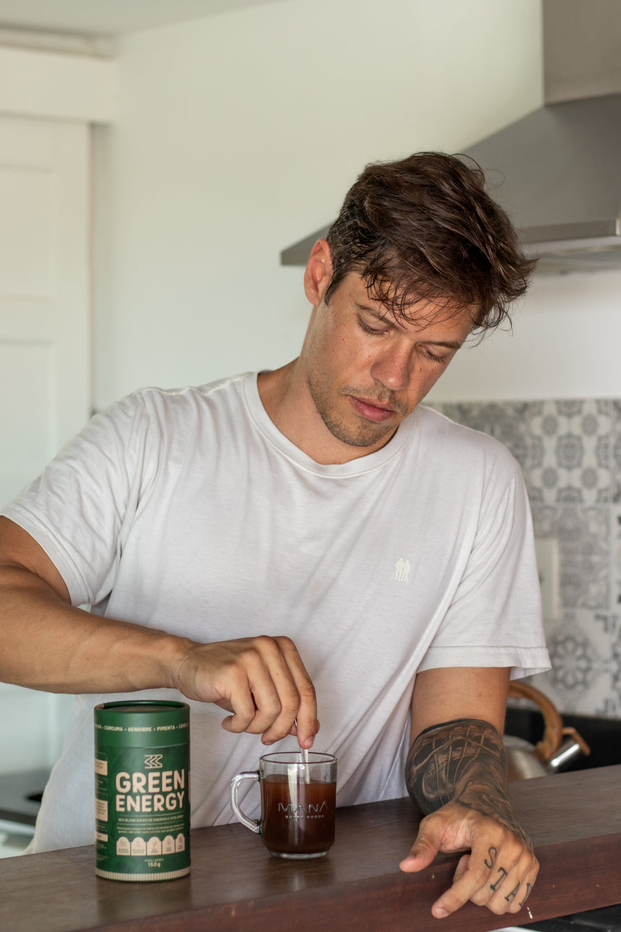 Fundador da Maná mexendo o Green Energy num copo de vidro, com a lata ao lado no balcão da cozinha