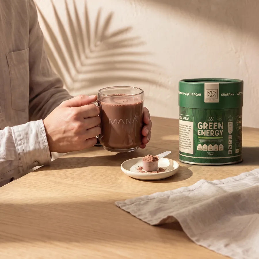 Mãos seguram a caneca de Green Energy de manhã, com a lata ao lado na mesa